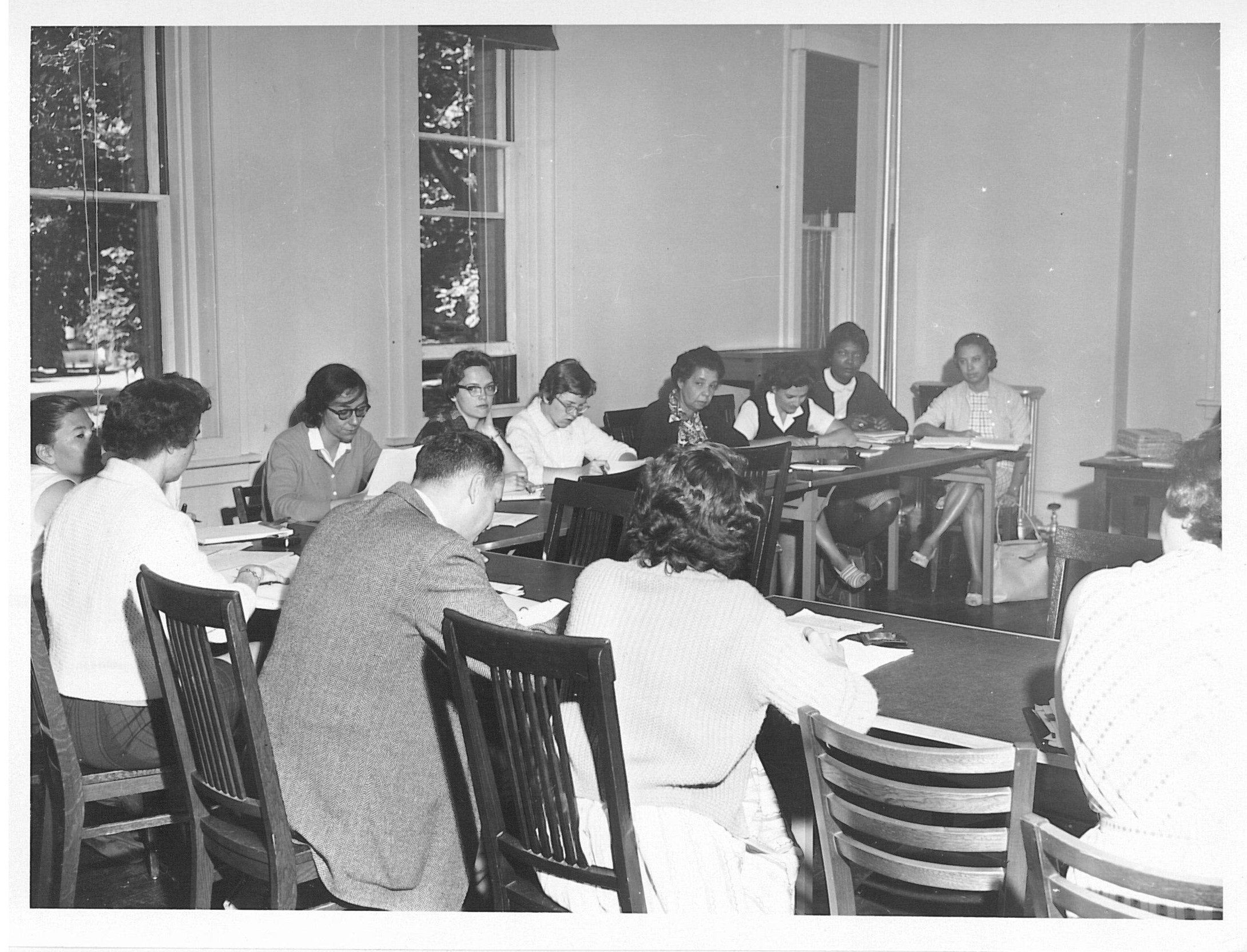 Black and white photo of people at an L shaped table in suits and dresses.